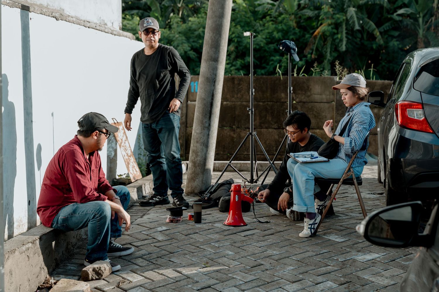 Film crew on location with camera equipment, four men working on an outdoor shoot near a white wall.