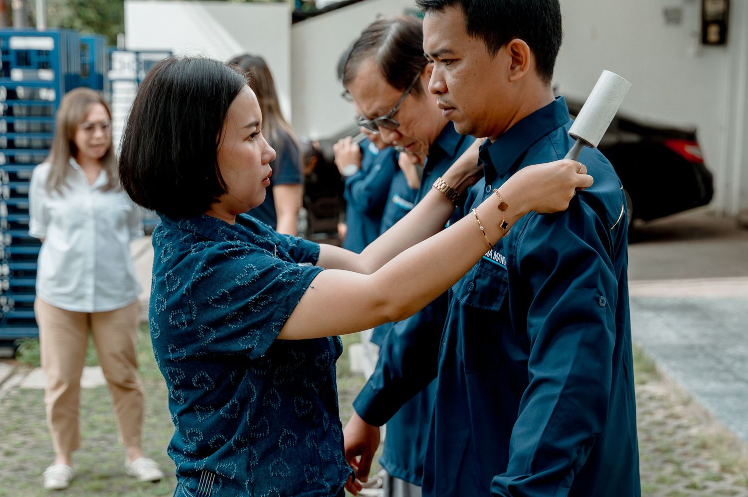 Woman adjusting man's teal shirt collar outdoors while others stand nearby in matching blue outfits.
