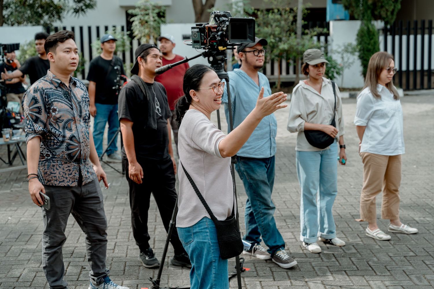 Film crew on outdoor set with director gesturing while camera operator and team observe during production.