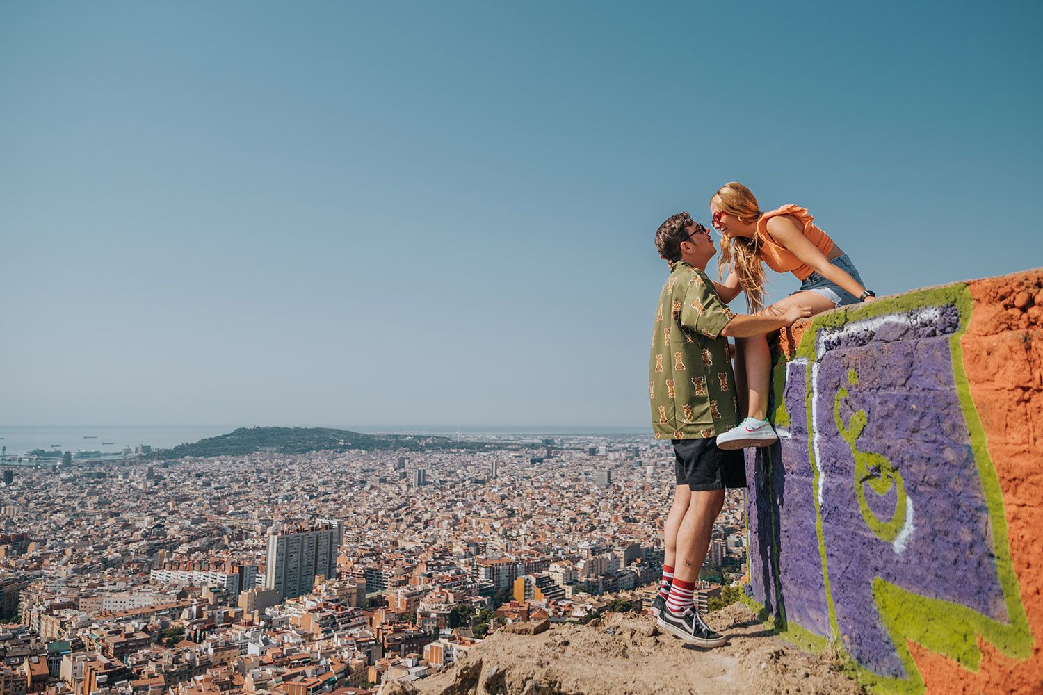 Laughing couple holding hands at Carmel Bunkers viewpoint for a private, candid Barcelona photo session.