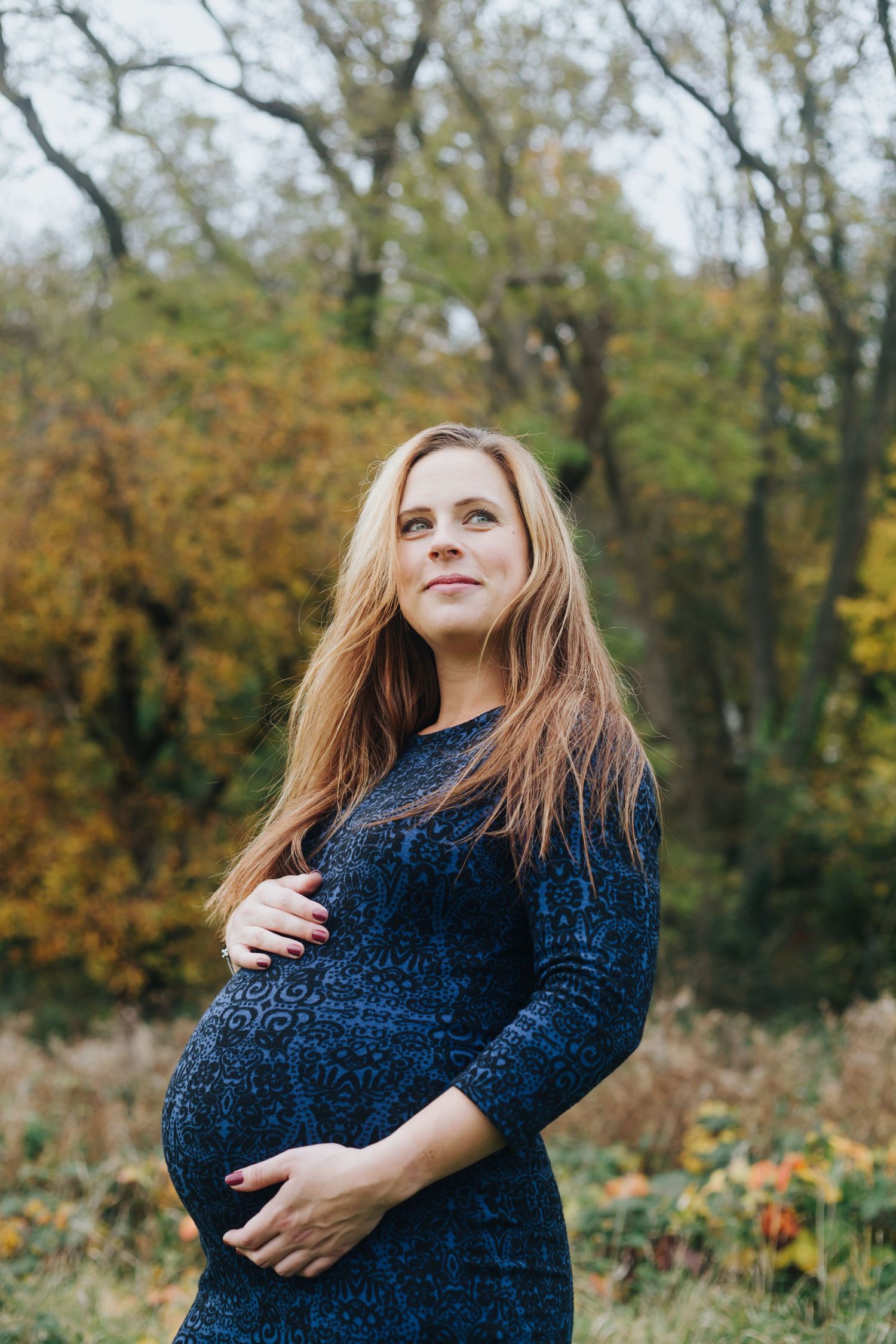 Pregnant woman standing in an autumn park during an outdoor maternity photography session.