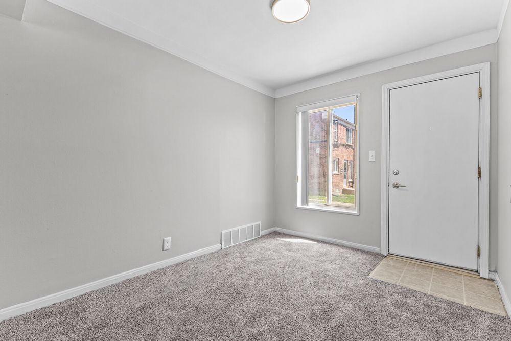 Empty room with gray carpet, white walls, and a front door with a window letting in natural light.