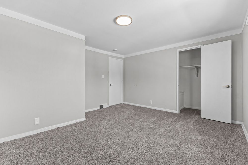 Spacious bedroom with gray carpet, crown molding, white walls, and open closet with built-in shelving.