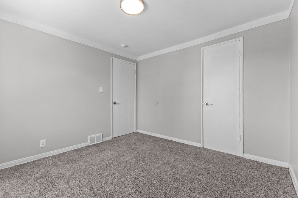 Empty bedroom featuring plush gray carpet, crown molding, two white doors, and light gray walls with a flush mount ceiling light.
