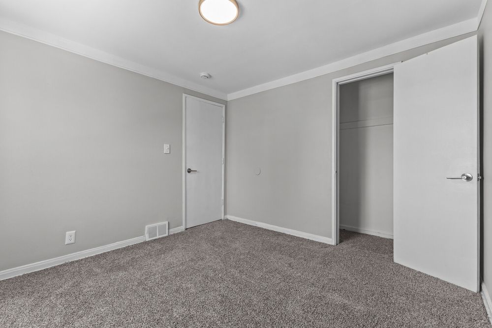 Empty bedroom featuring gray carpet, crown molding, white walls, and a walk-in closet with open door.