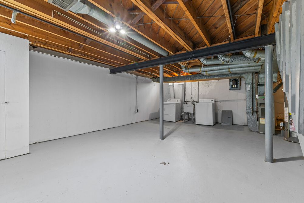 Unfinished basement with exposed wood ceiling joists, painted concrete floor, and utility equipment.
