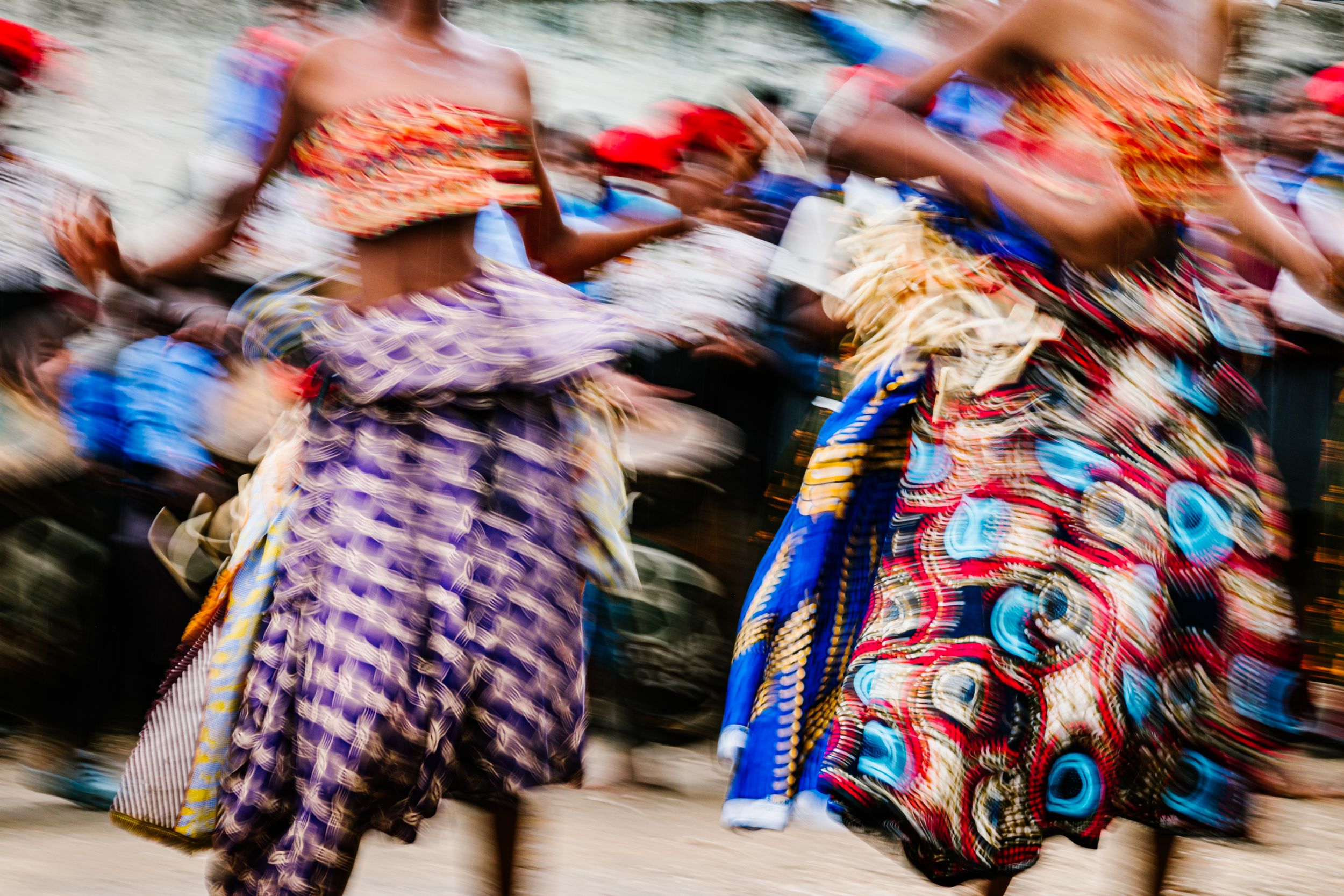 Vibrant motion blur of African women dancing in colorful traditional patterned fabric dresses during a cultural celebration.