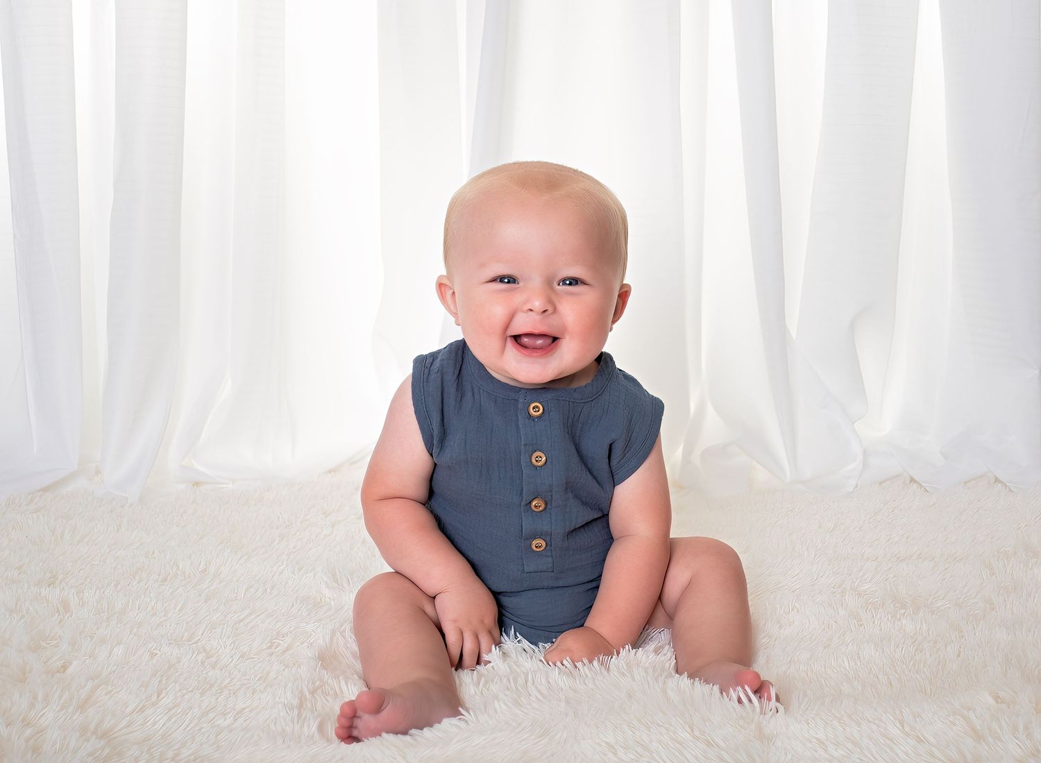 Baby sitting on white fur with a gray elephant and brown fox stuffed animals against a white background.