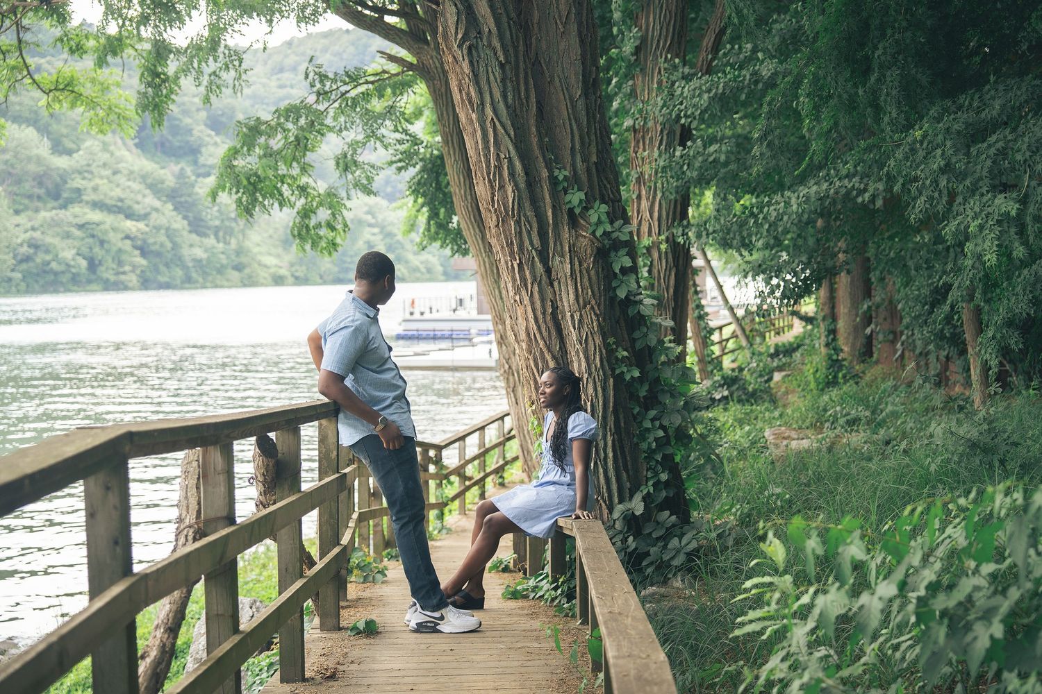 Couple enjoying a scenic riverside wooden walkway surrounded by lush green trees and tropical foliage.