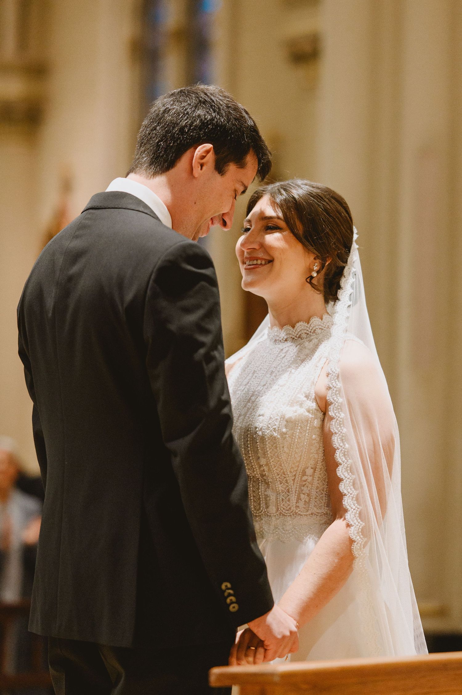 Bride and groom holding hands and smiling at each other during a church wedding ceremony.