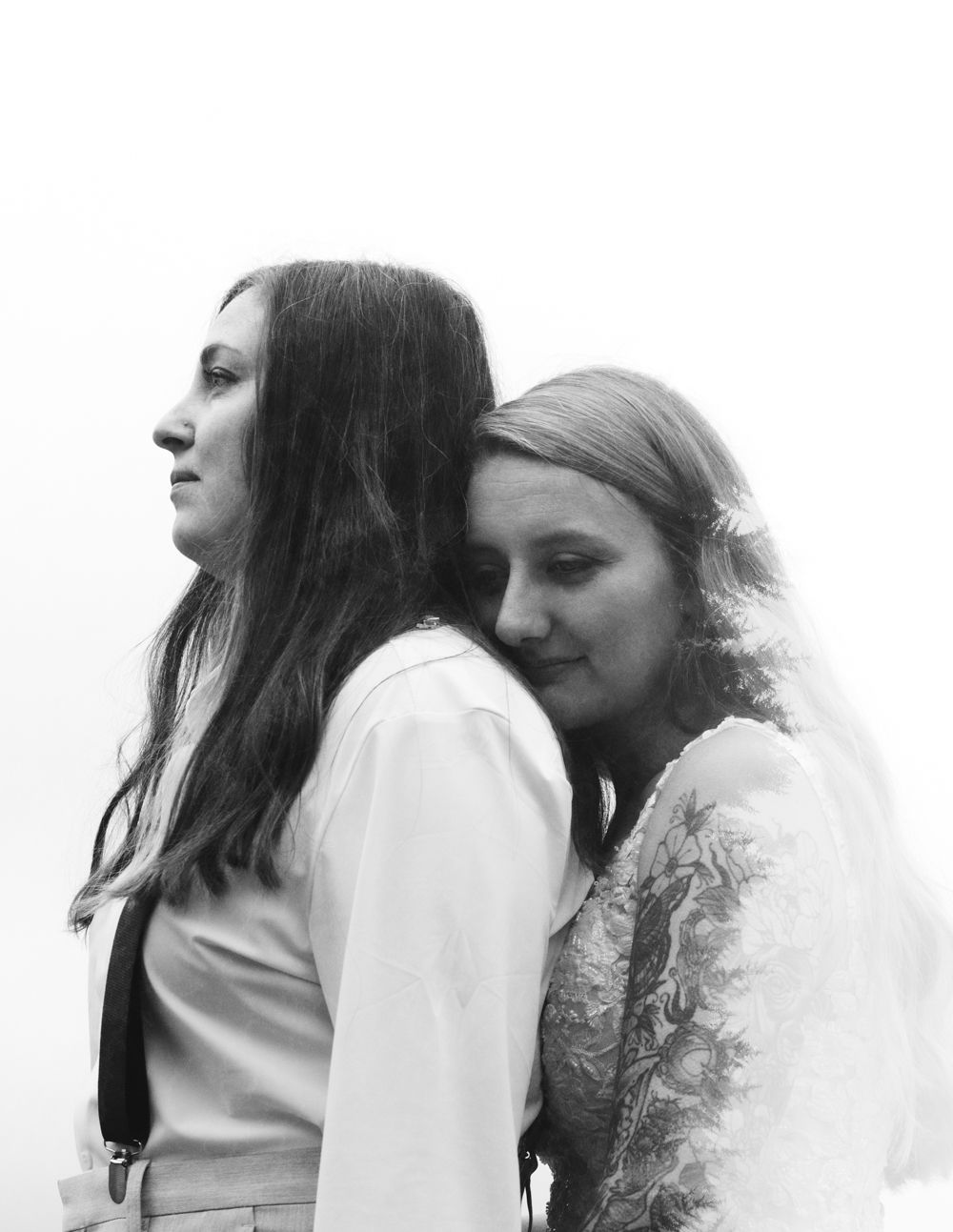 A double exposure in black and white of a LGBTQ couple embracing on their wedding day, with tops of the fir trees overlaying her long hair