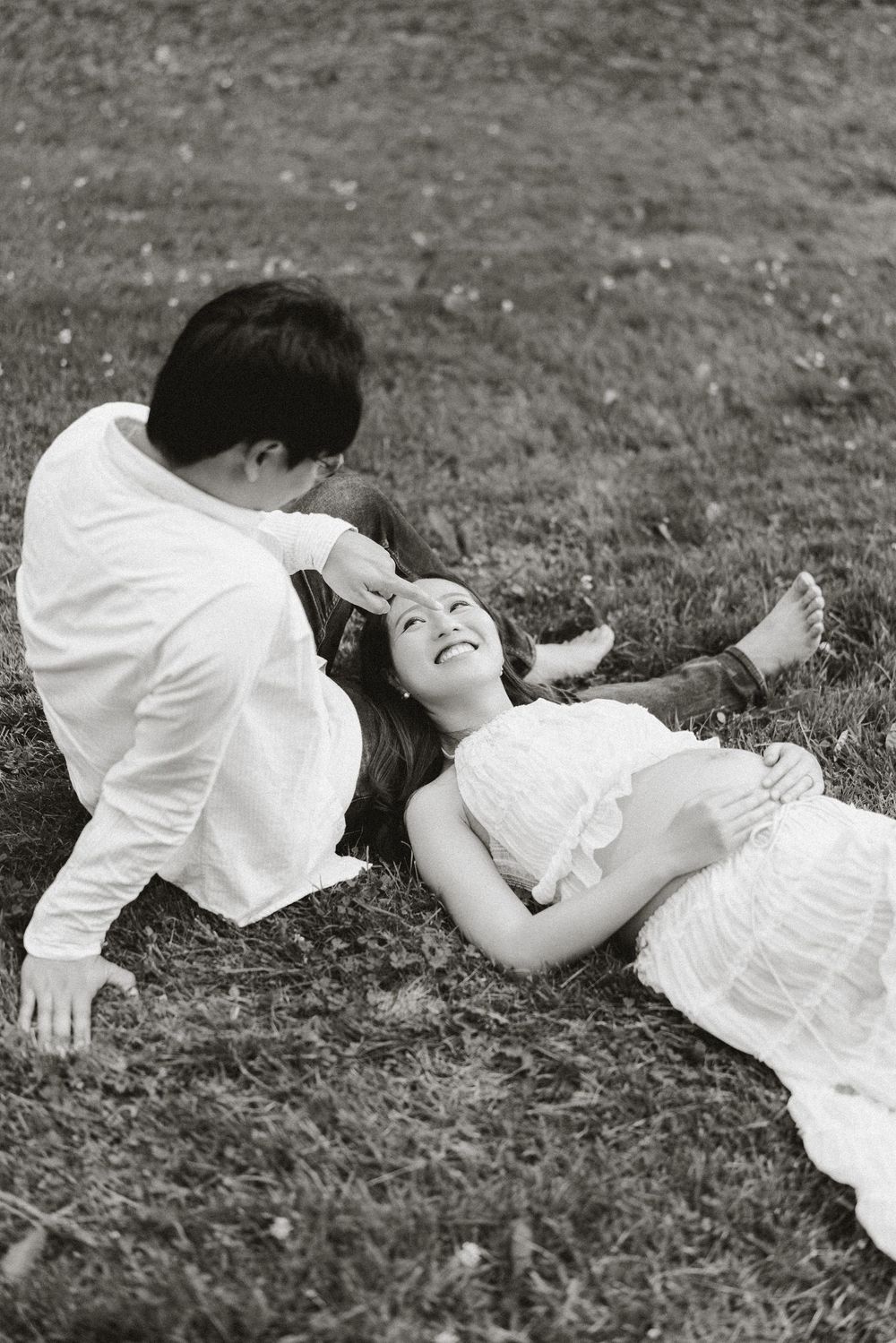 Expectant mother lying on the grass with her partner leaning over her, black and white.