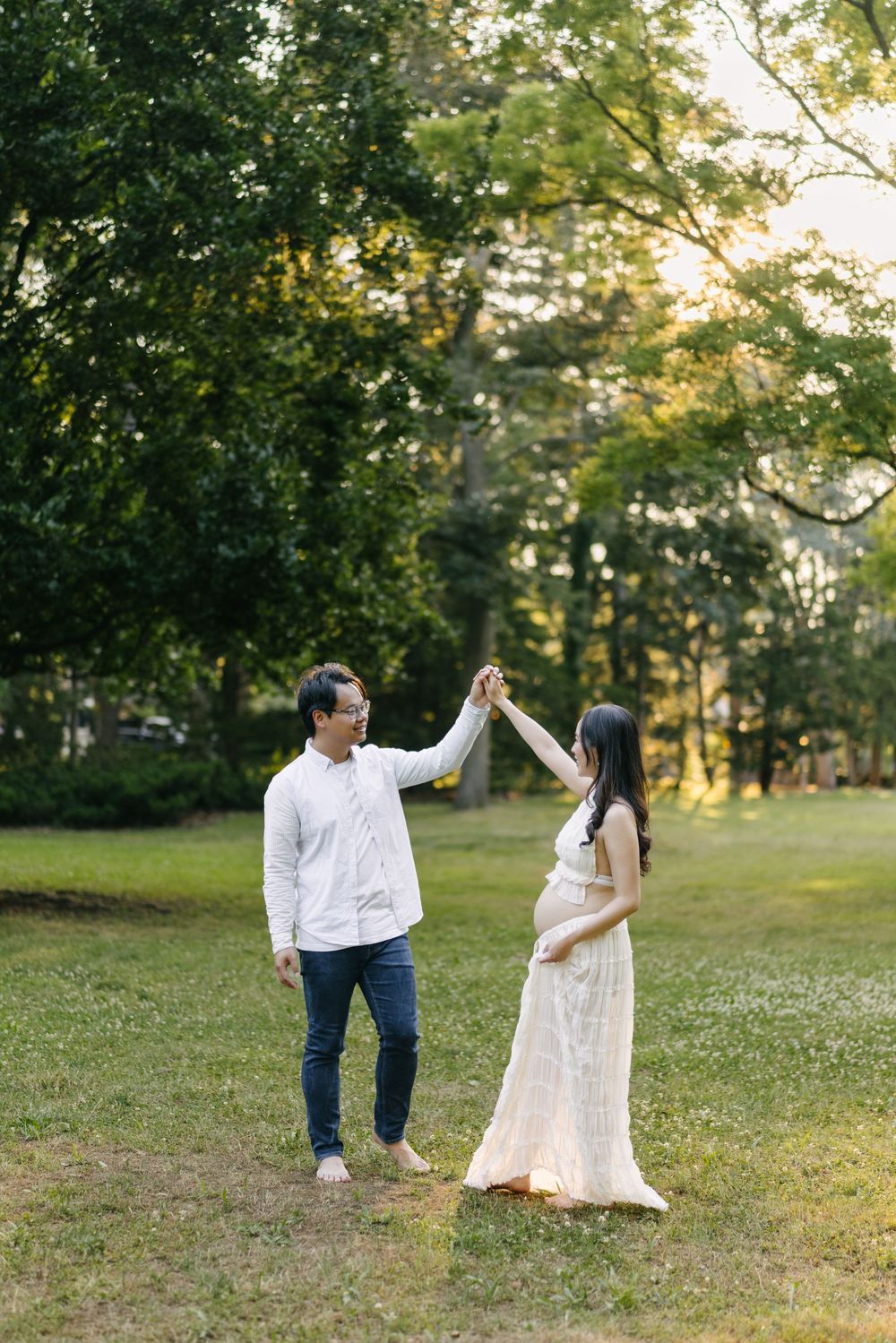 Expectant couple dancing under raised hands on a grassy slope.