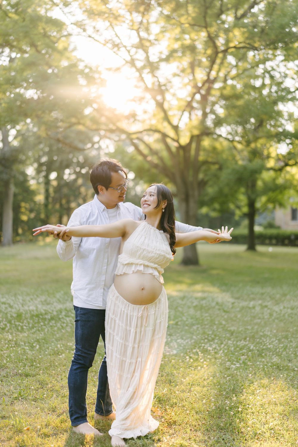 Partner spinning the expectant mother in a park at sunset.