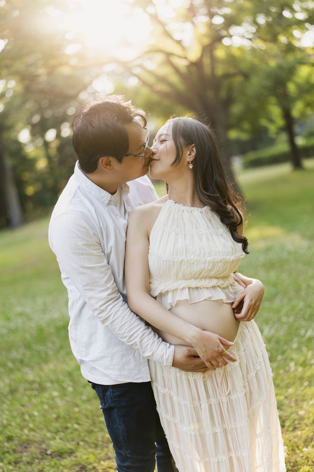 Expectant couple embracing in a park at golden hour.