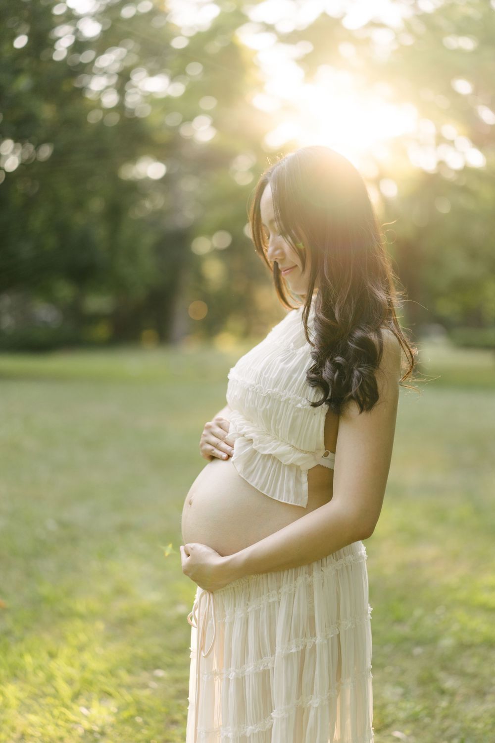 Expectant mother cradling her belly in golden evening light.