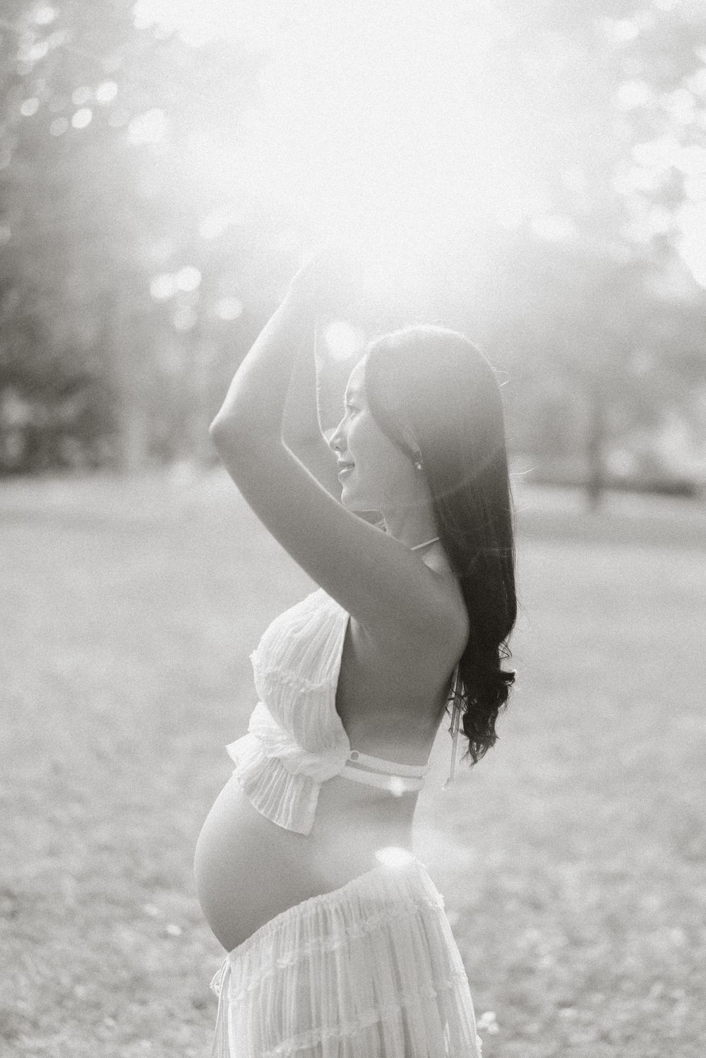 Expectant mother arching back in soft backlight, black and white.