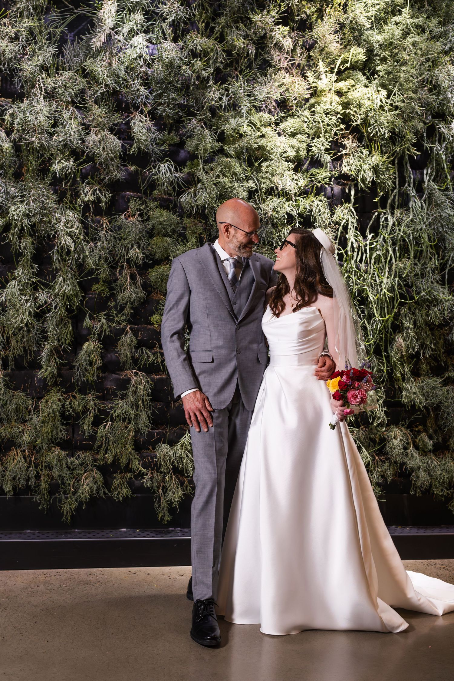 Bride and groom share a romantic moment in front of a lush green living wall on their wedding day.