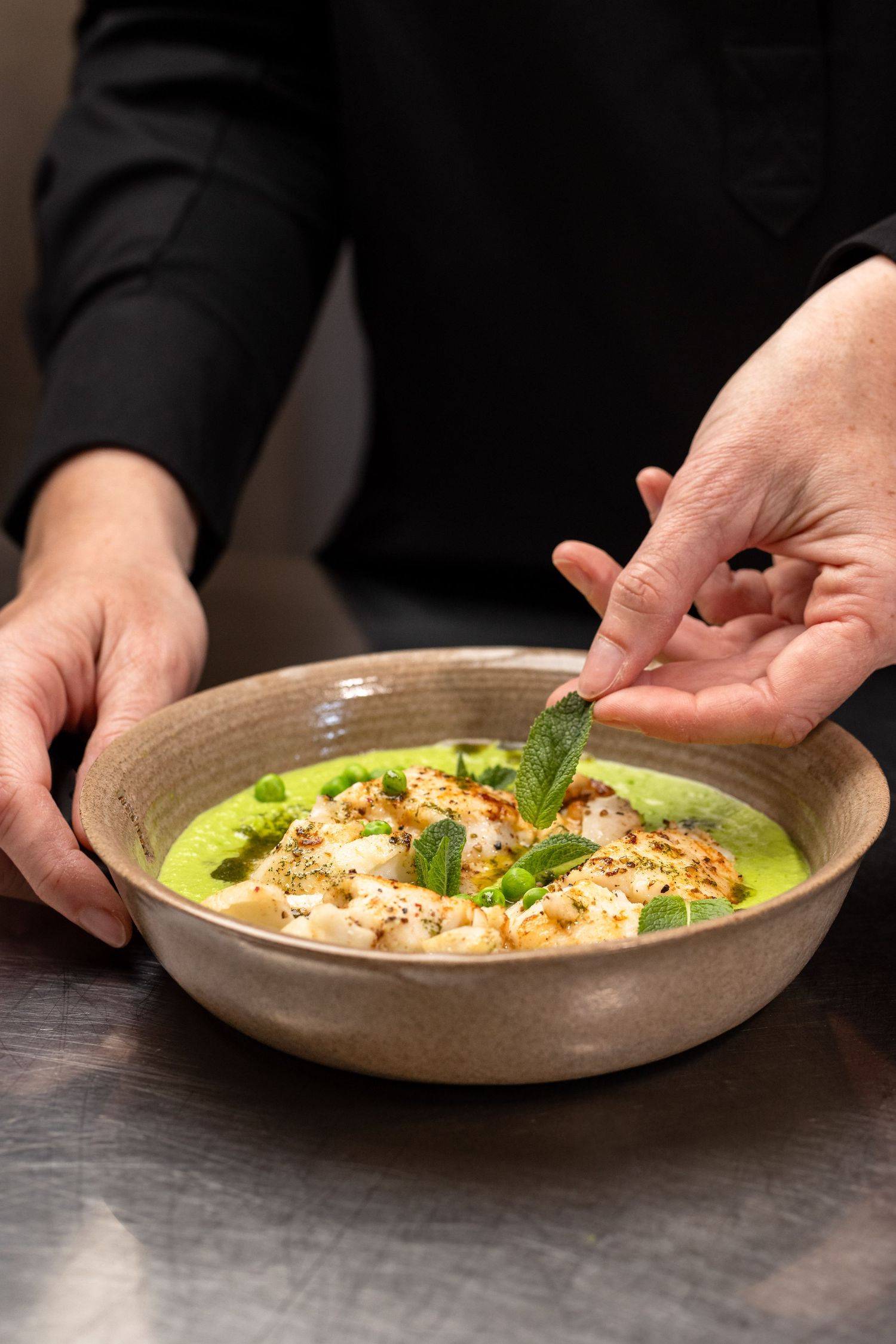 Person pouring orange vegetable soup from bottle into ceramic bowl, surrounded by fresh parsnips, pumpkin, and leeks.