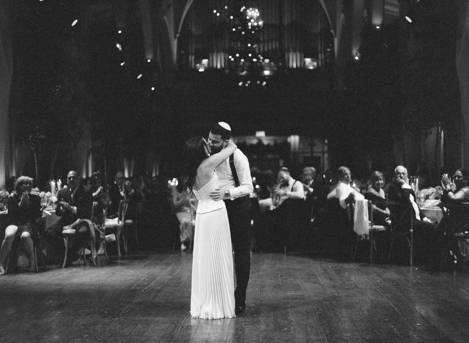 Black and white photo of a couple sharing their first dance at a wedding reception in an elegant hall.