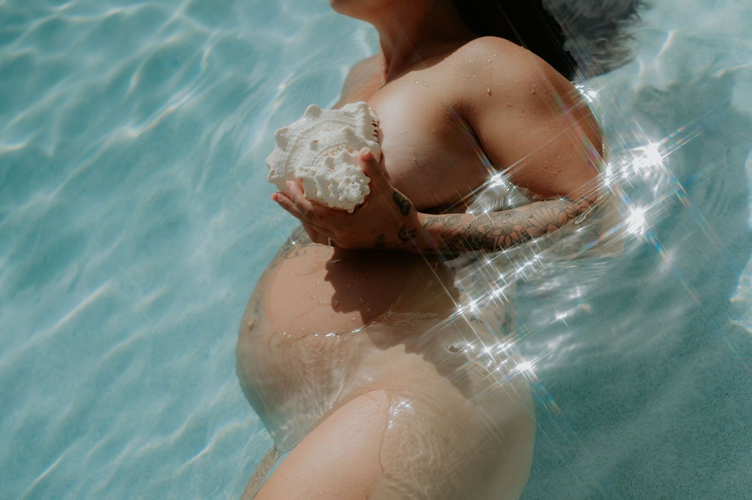 Underwater maternity photography with shell on the Sunshine Coast in heated pool with sun sparkles lens with flares