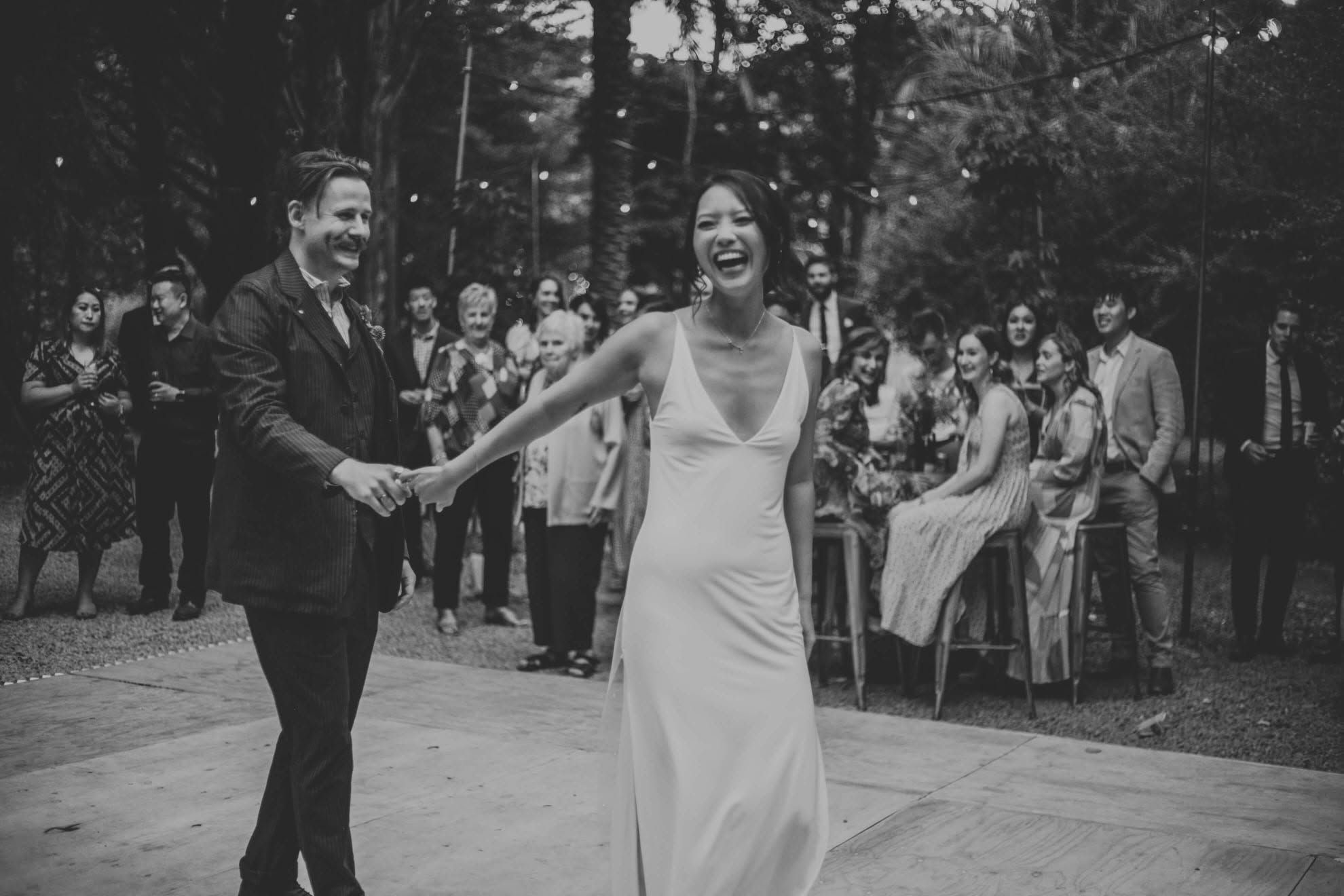 Joyful newlyweds walking hand in hand through a confetti shower under lush green weeping willow trees.