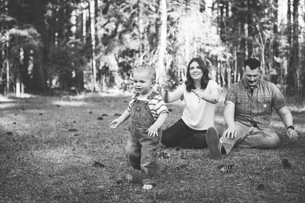 Black and white photo of a young family with a toddler playing outdoors in a forest setting.