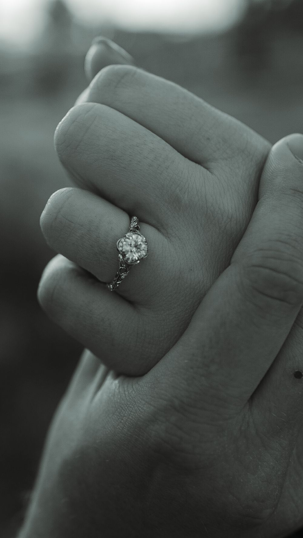 Close-up black and white photo of a hand wearing a stunning diamond solitaire engagement ring with decorative band.