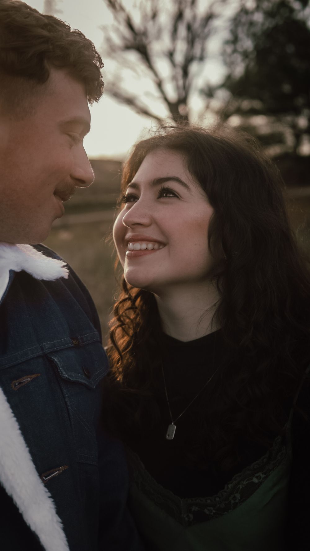Happy young woman smiling at her partner during a romantic outdoor engagement session at sunset.
