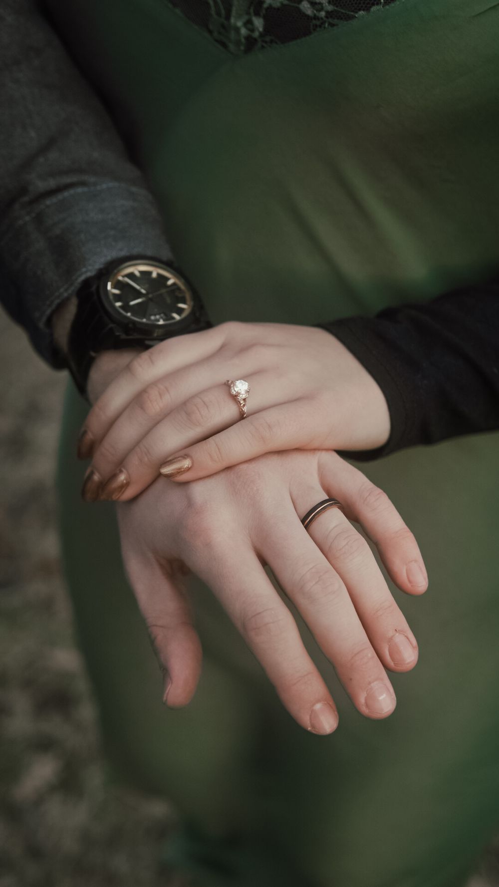 Close-up of a couple's hands showing an engagement ring and wedding band, with a black watch visible on the man's wrist.