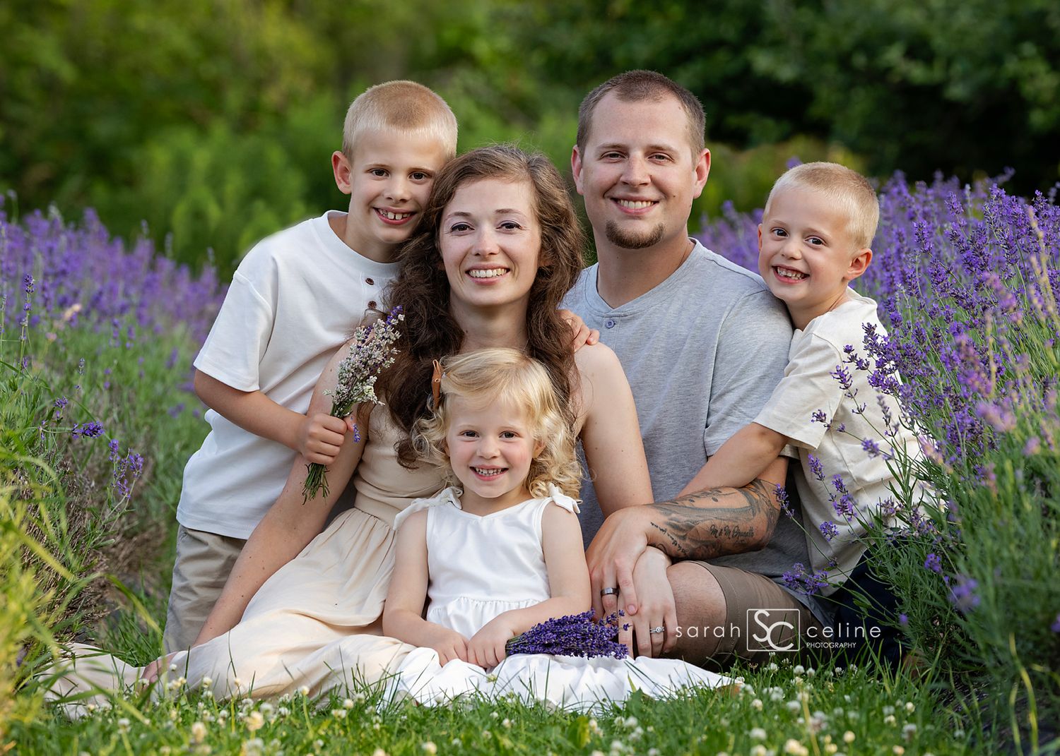 Happy family of five posing in a blooming lavender field, parents with three young children smiling outdoors.