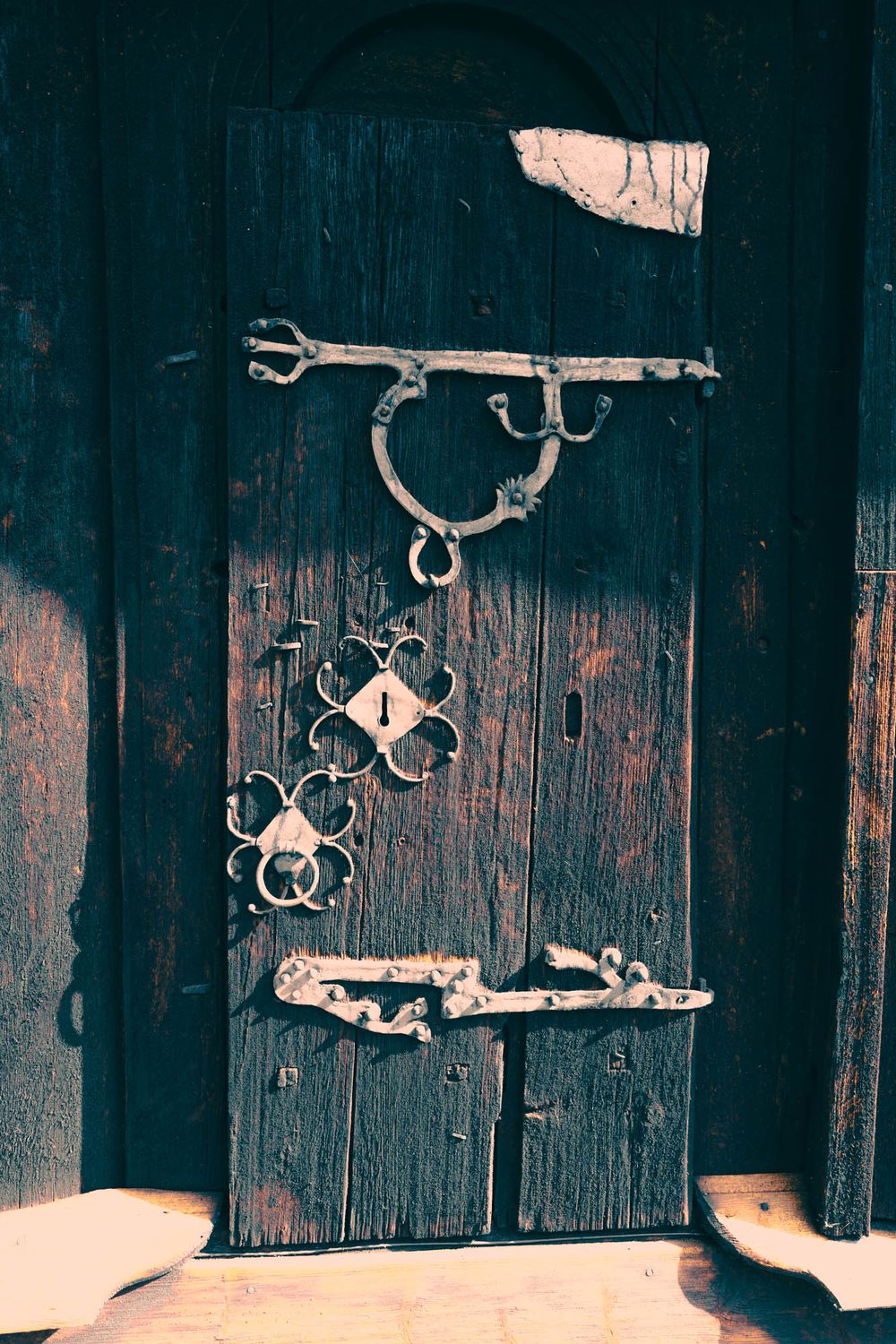 Ancient dark wooden door with ornate wrought iron hardware, floral lock plate, and decorative hinges on a historic building.