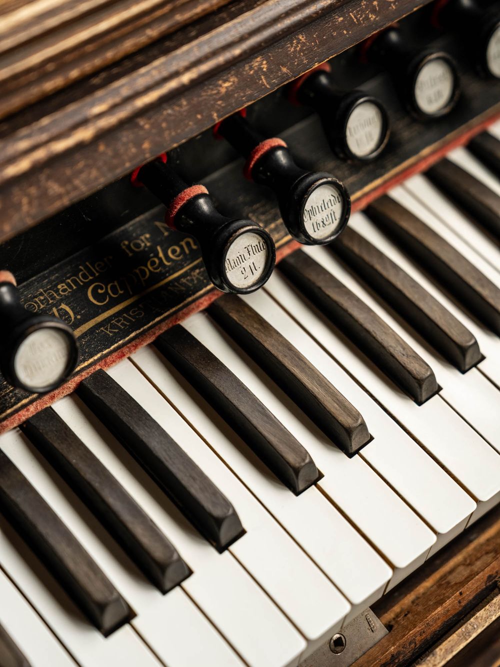 Close-up of antique organ keyboard with ivory keys, black stops, and ornate wooden casing showing aged patina.