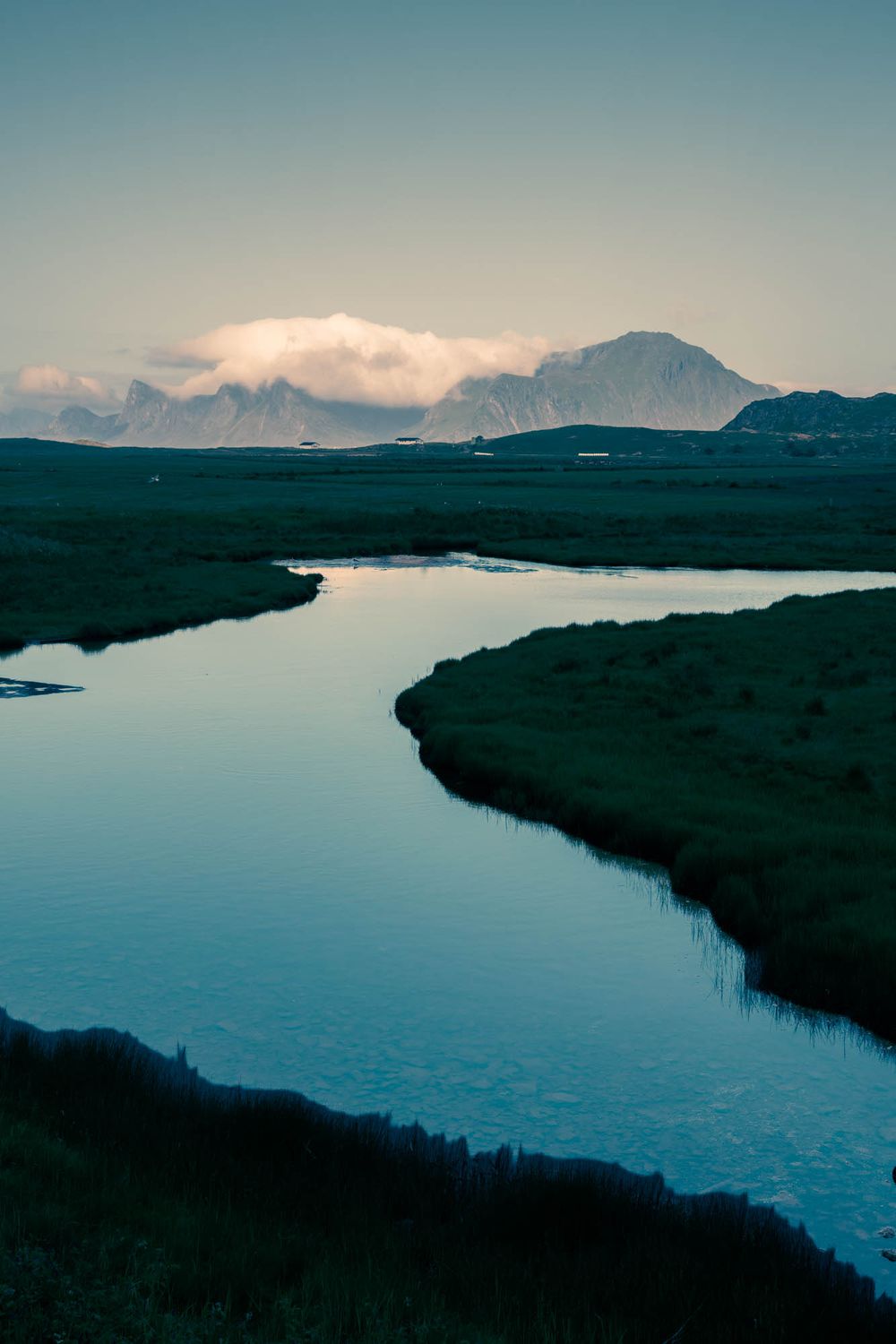 A winding river reflects the twilight sky through a lush green valley with misty mountains in the distance.
