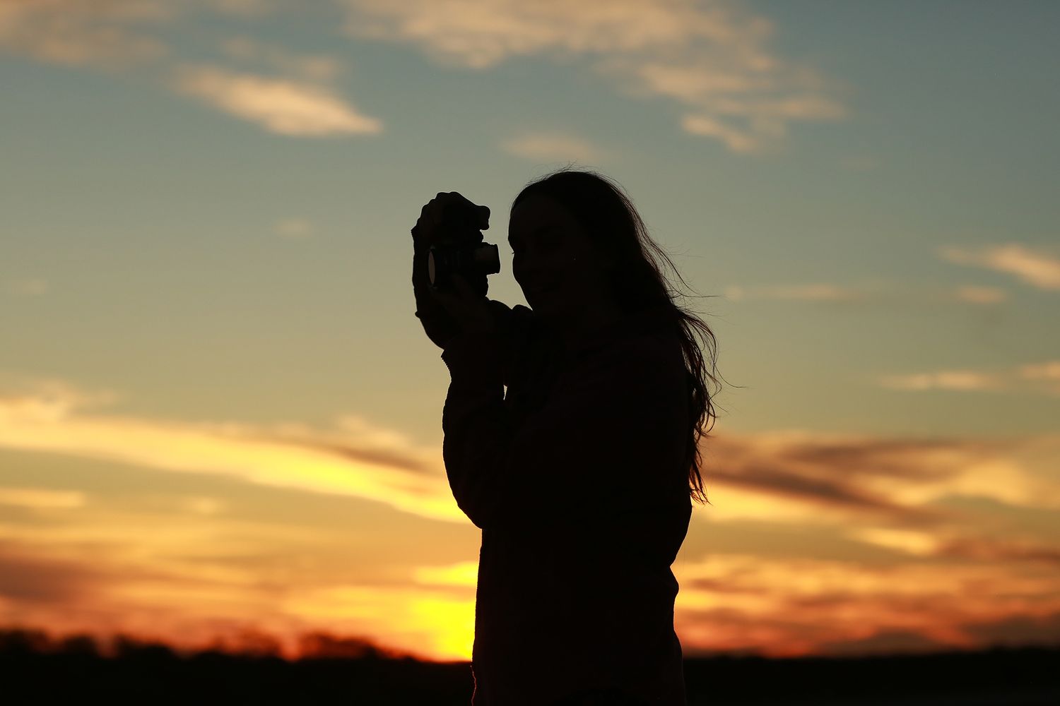 Silhouette against western australian sunset of a girl looking through viewfinder of her camera