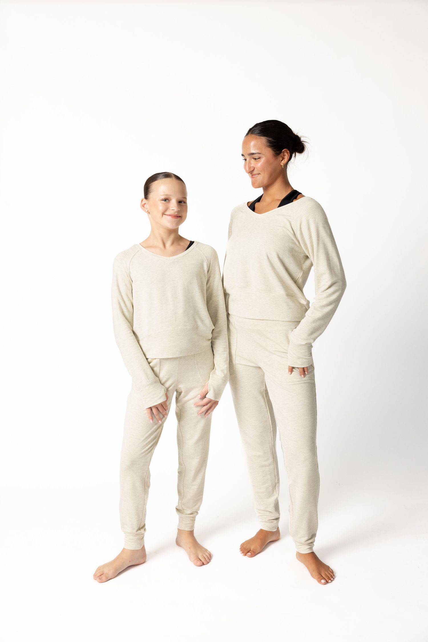 A woman and young girl wearing matching cream-colored loungewear sets with long sleeves and jogger pants on white background.