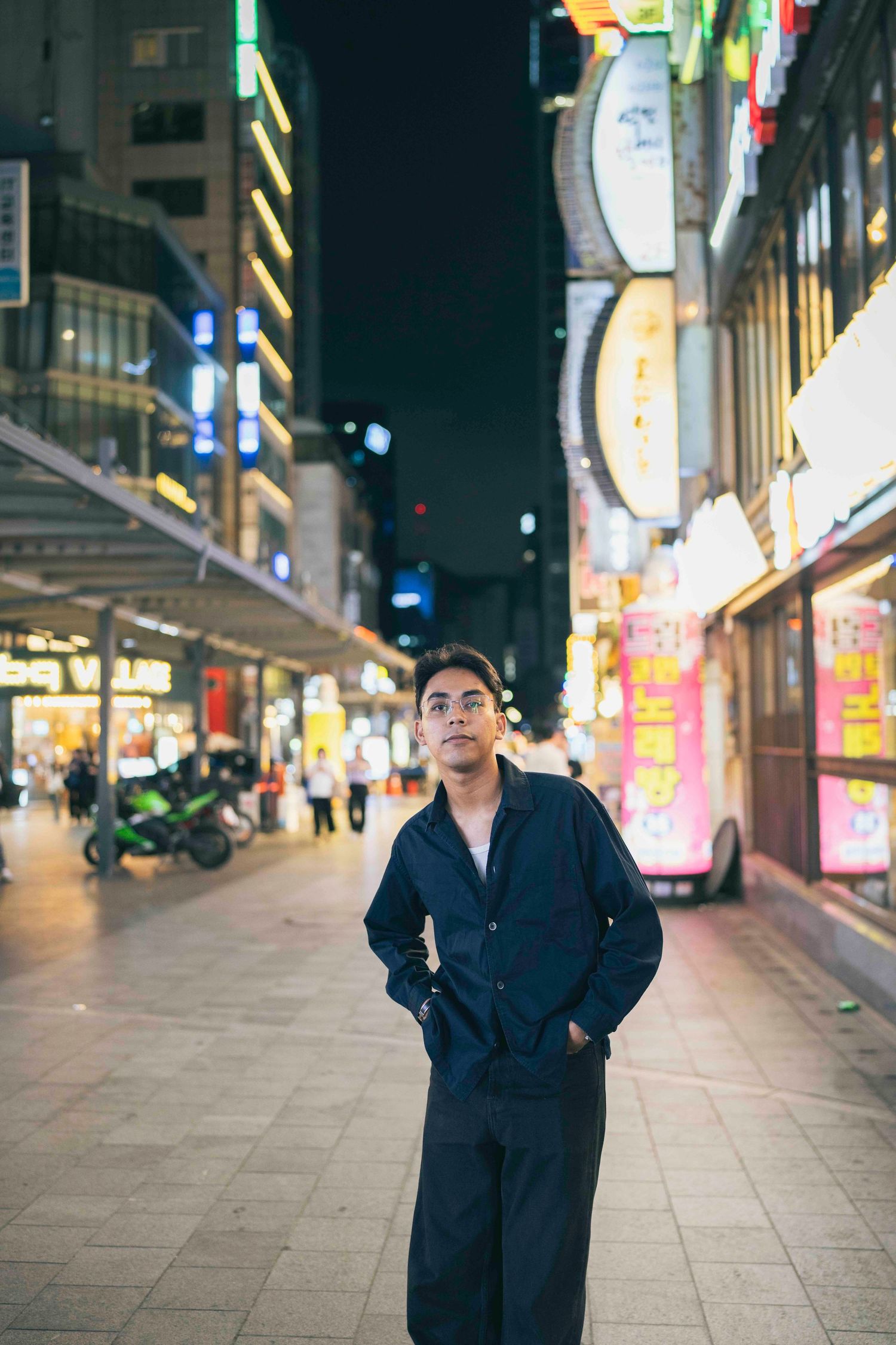 Couple smiling and posing on a vibrant night street in Seoul, South Korea, surrounded by neon signs.