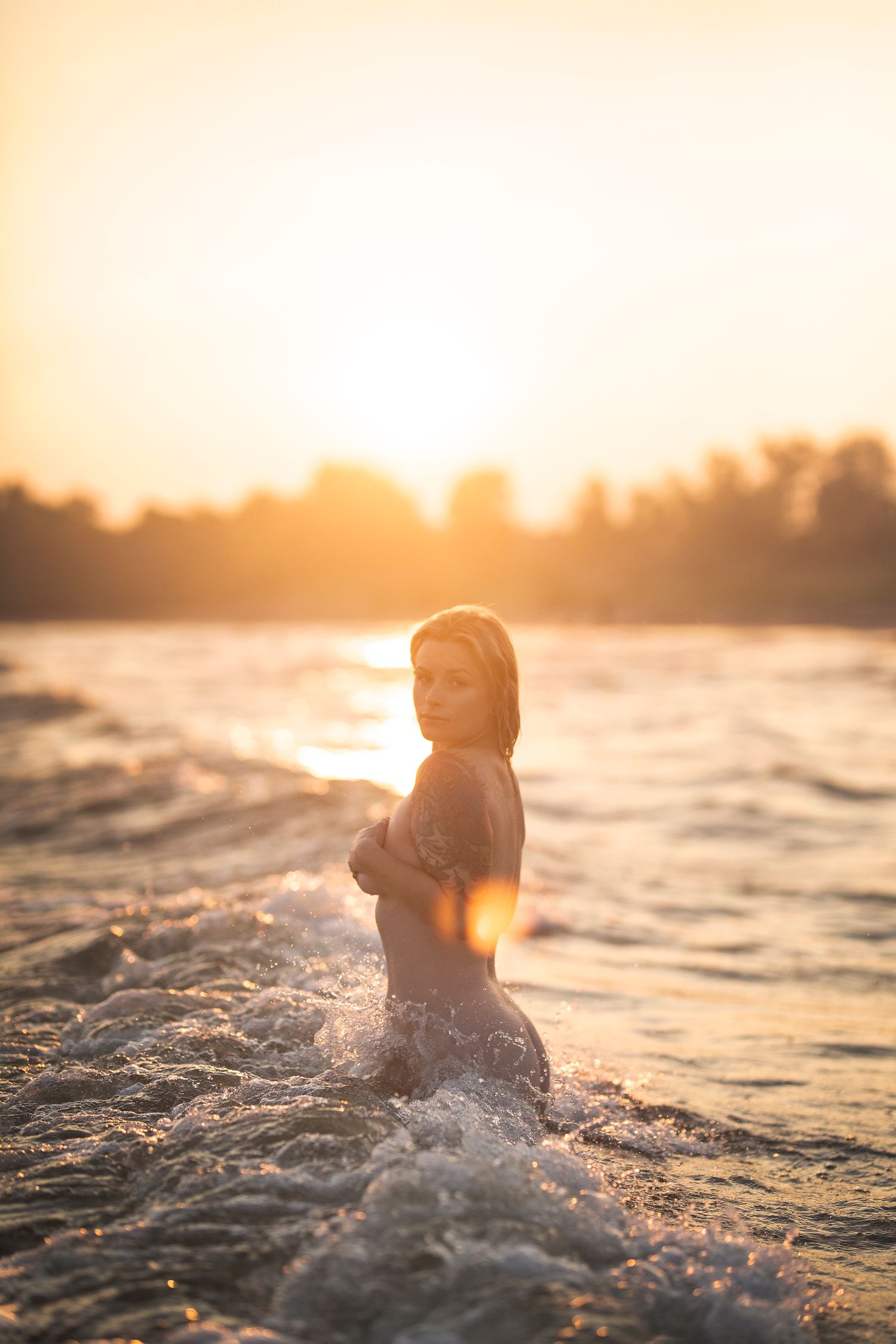 Person standing in ocean waves at sunset with warm golden lighting.