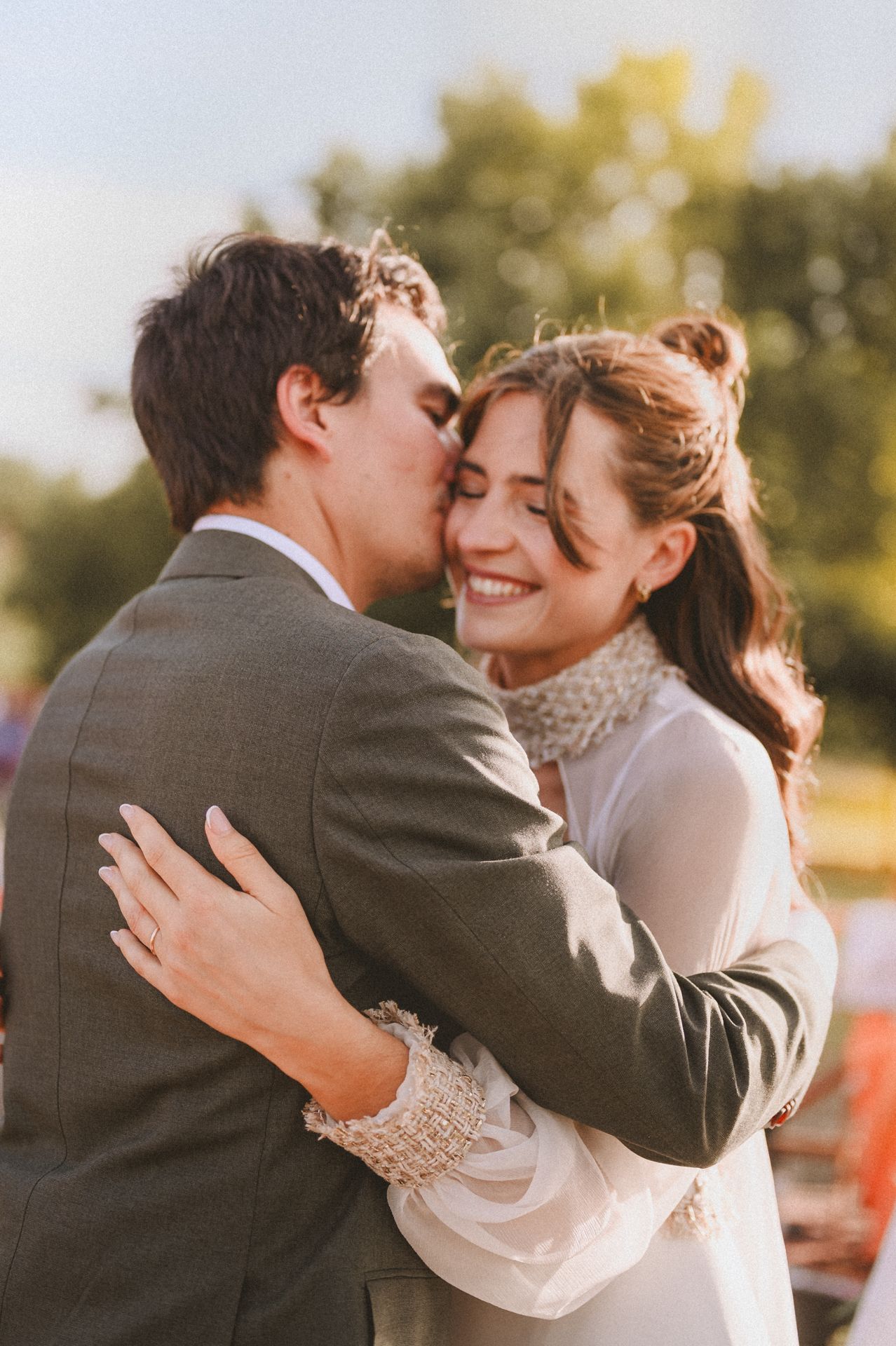 Groom kisses smiling bride on the cheek during a golden hour outdoor wedding ceremony.