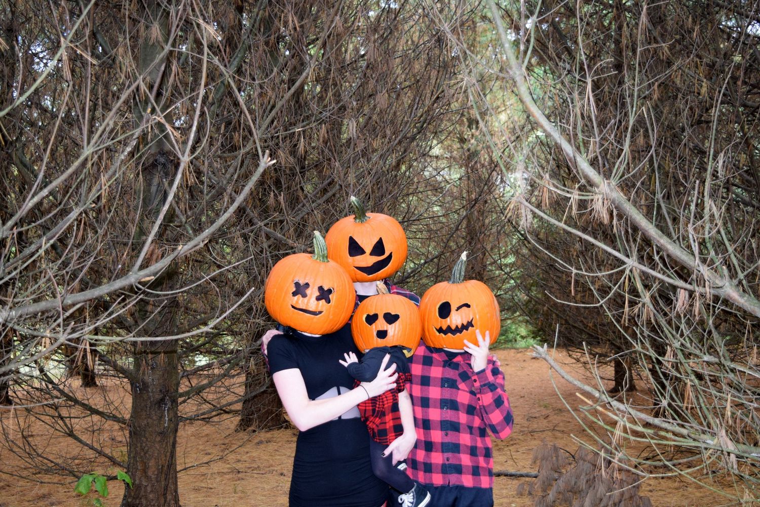 Family wearing orange jack-o-lantern pumpkin head masks posing in a spooky forest for Halloween.