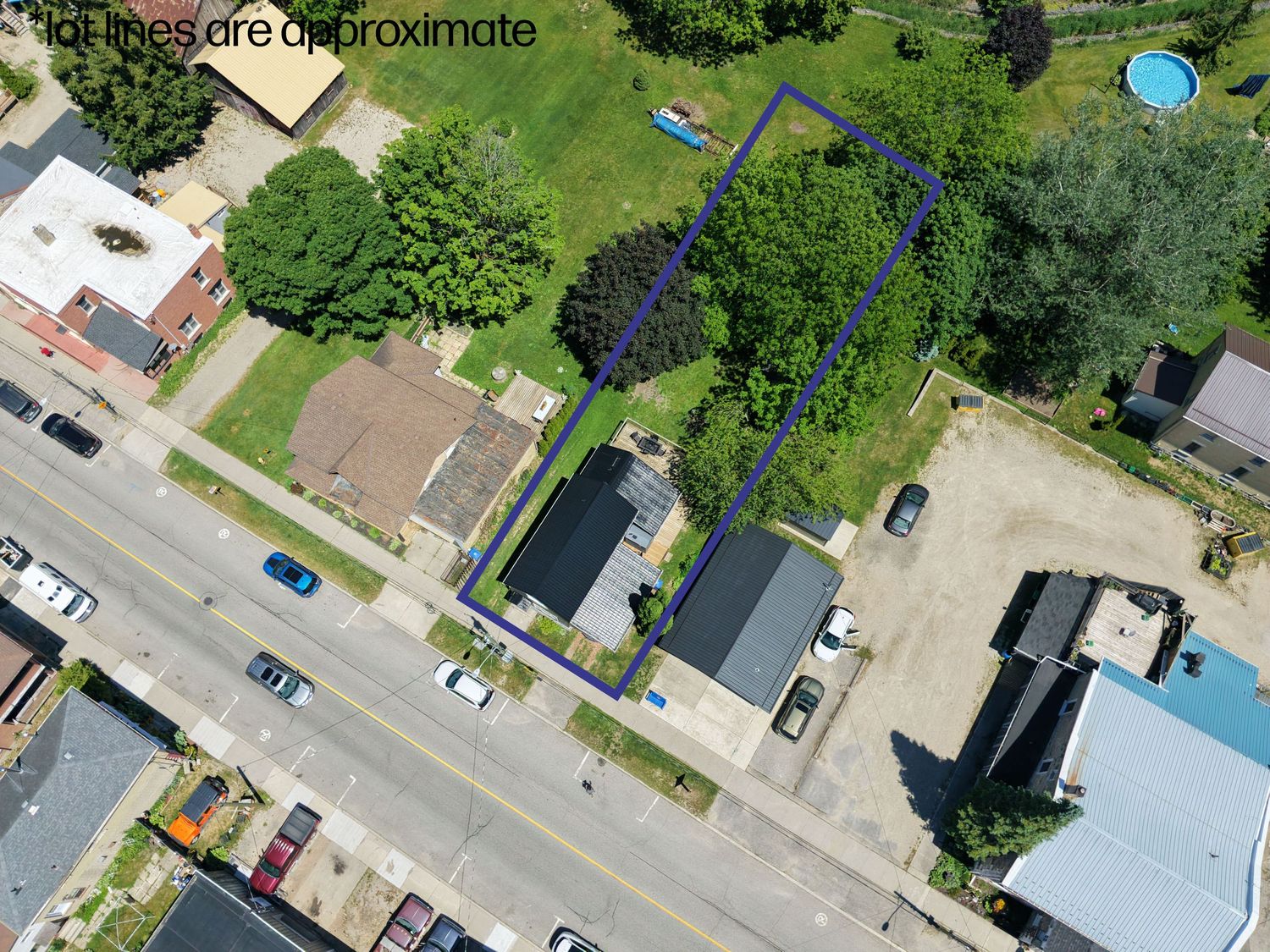 Aerial drone view of a residential property with outlined lot lines, featuring a house, large trees, and surrounding neighborhood streets.