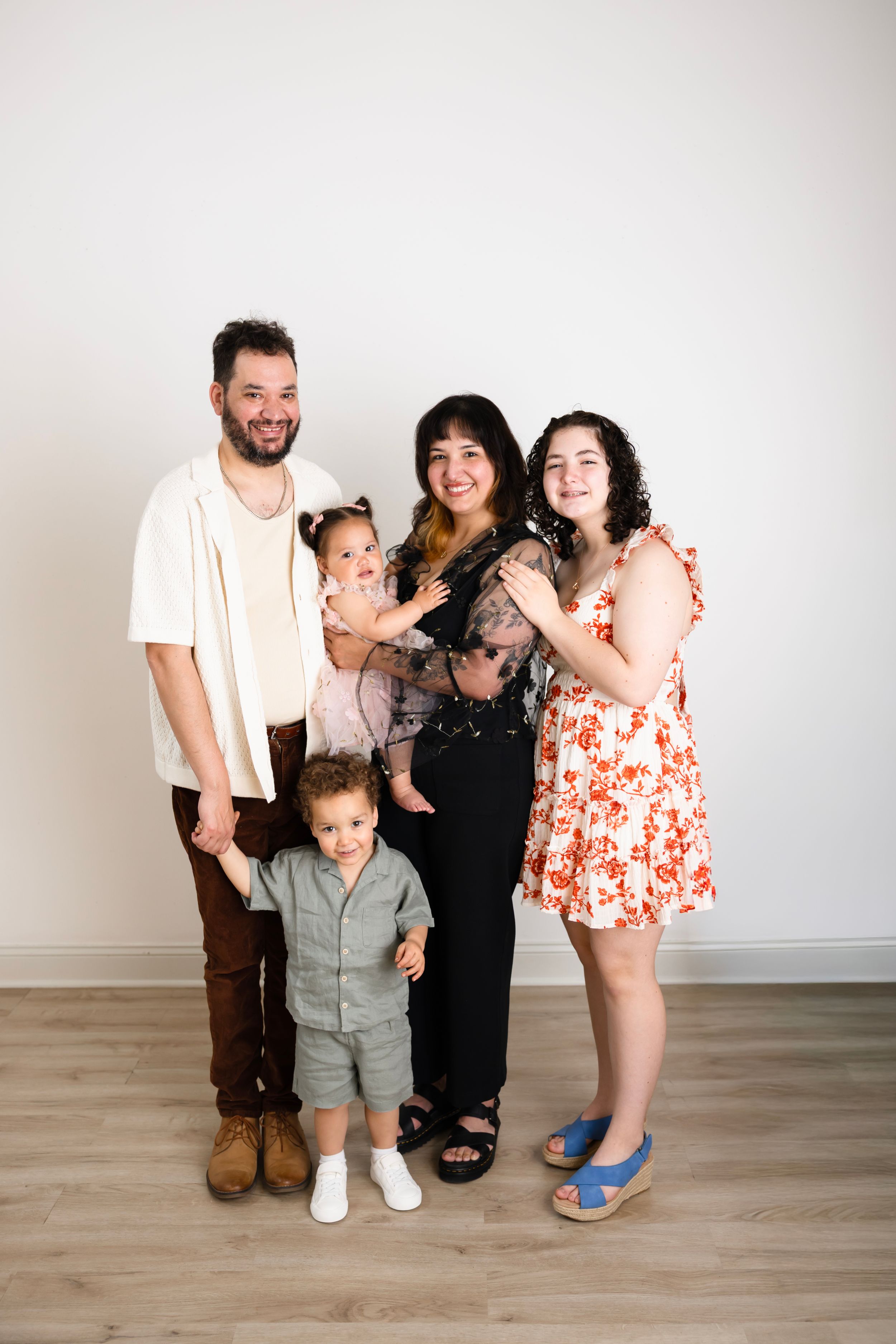 A joyful family of five posing together in a bright studio, including two young children and three adults in casual attire.