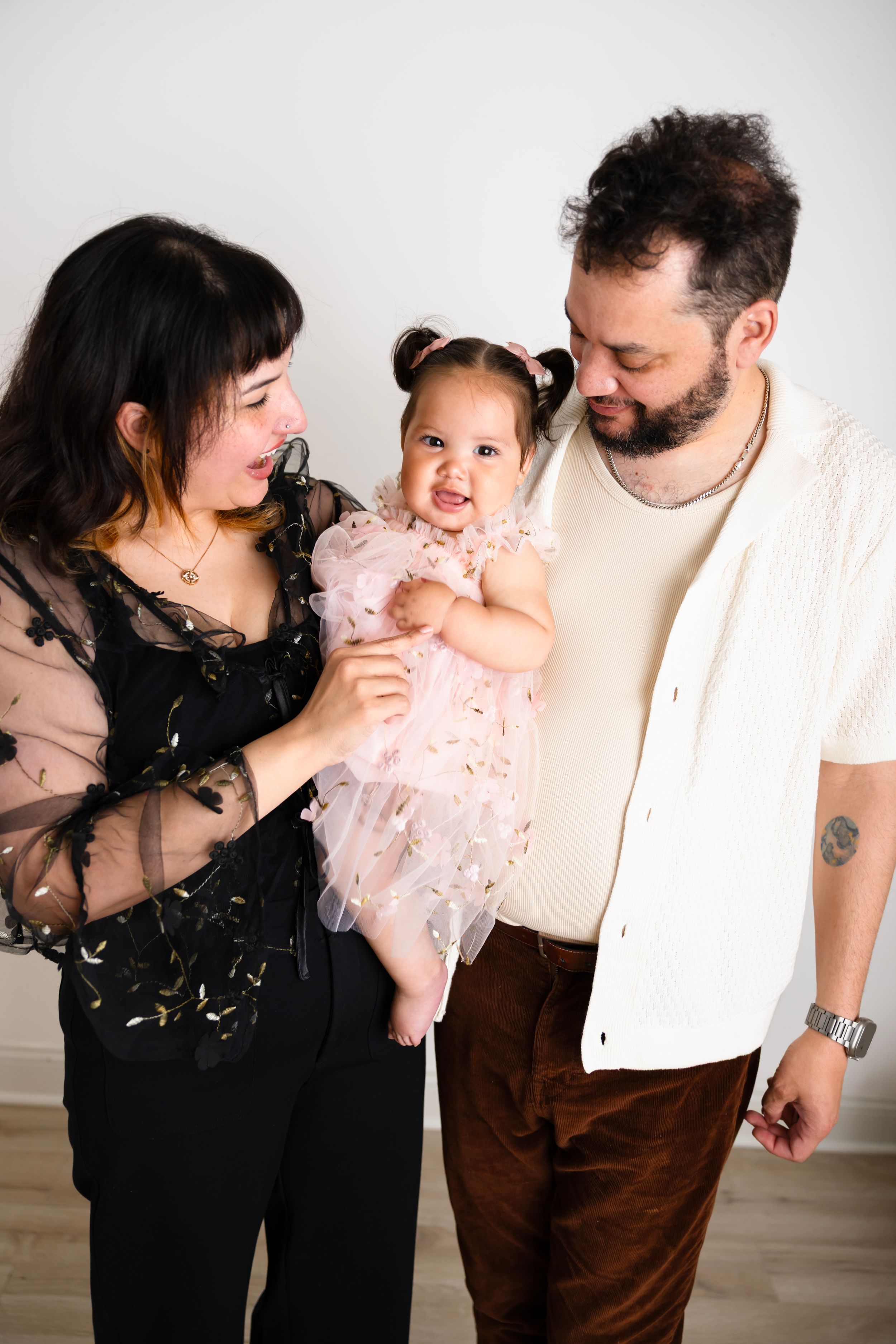 Happy parents admiring their smiling baby girl in a pink tutu dress during a family photo session.