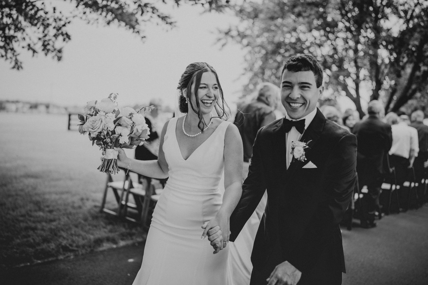 Happy newlyweds walk down the aisle smiling after their outdoor wedding ceremony in black and white photo.