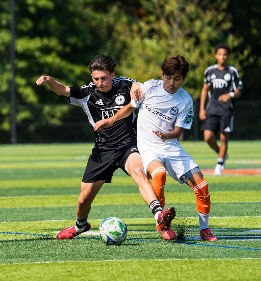 Two youth soccer players battle for the ball during a competitive match on a green turf field.