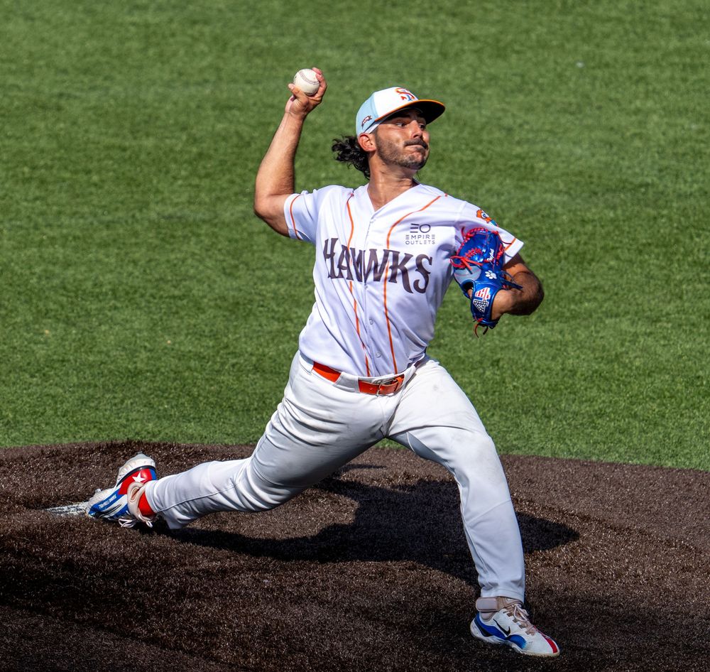 Hawks baseball pitcher in white uniform mid-windup on mound, preparing to throw during a sunny outdoor game.