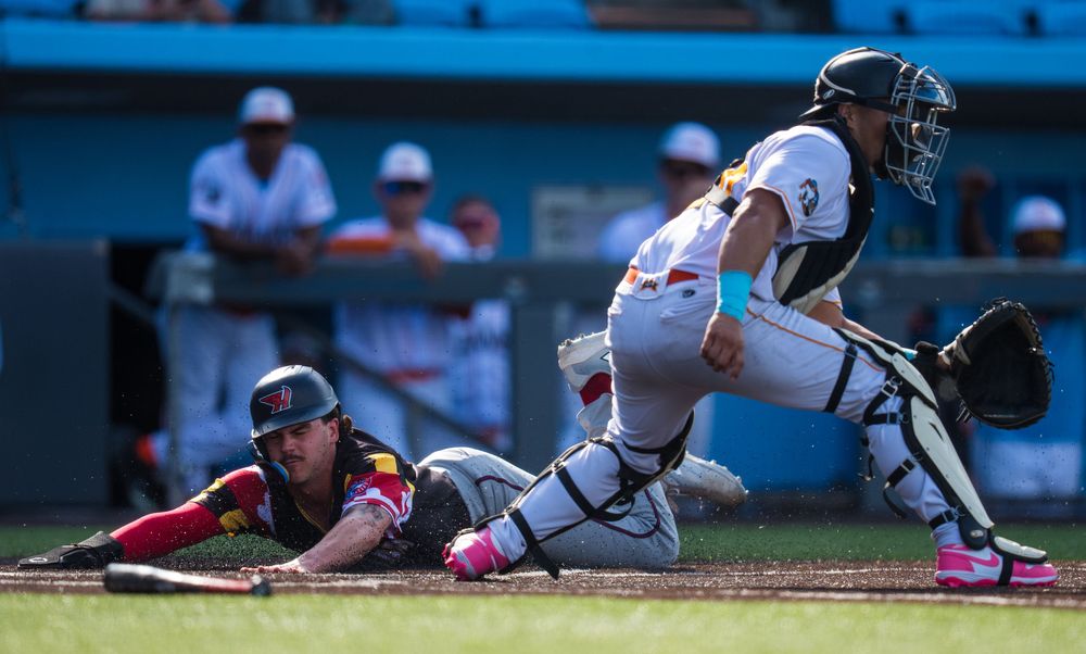 Baseball player slides into home plate as catcher attempts to make the tag during a game.