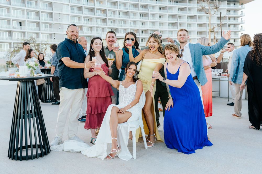 Group of friends posing together at a beachfront wedding reception, dressed in colorful formal attire.
