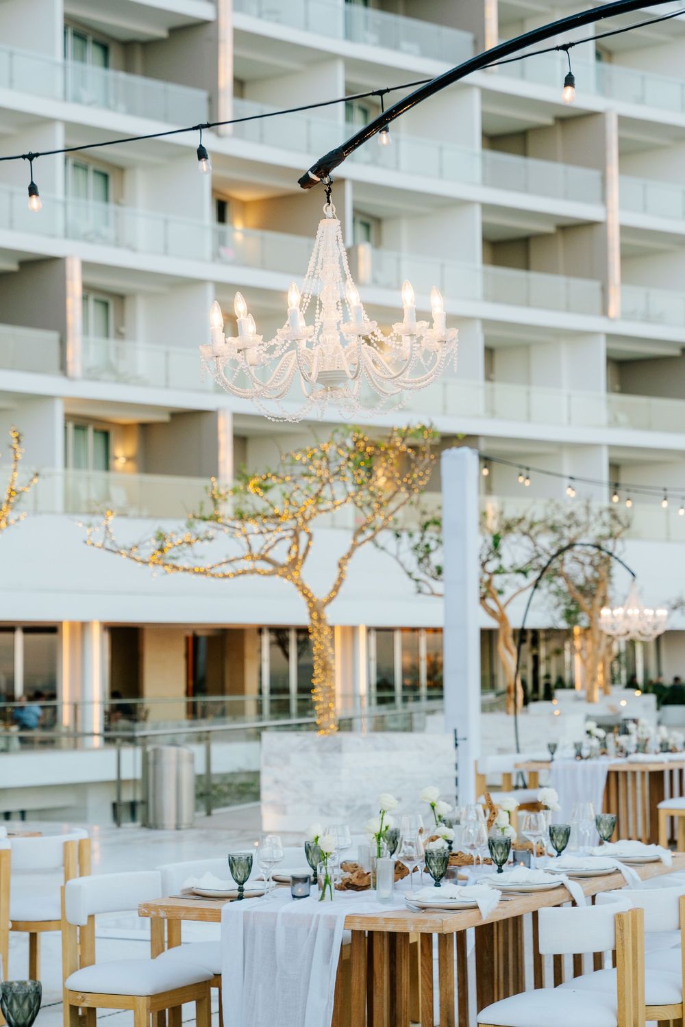 Elegant outdoor wedding reception with white chandeliers, string lights, and beautifully set tables at a resort.