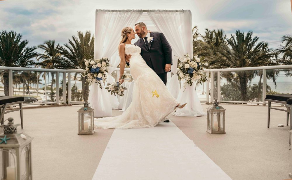 An elegant outdoor beach wedding ceremony with white decor and palm trees.